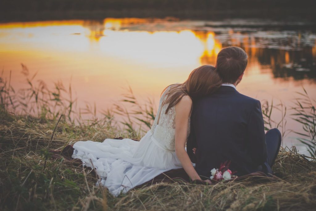 a man and woman kissing on a rock by a lake